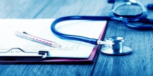 A doctors clipboard with a pen next to a stethoscope on top of a wooden table