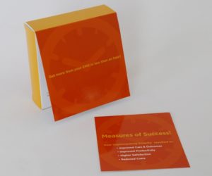 A standing bright orange clock box with a yellow back next to an orange informational paper that says measures of success