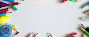 Colored pencils, thumb pins, crayons and white out set up in a circle on a white table