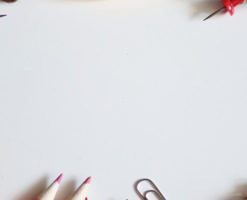 Colored pencils, thumb pins, crayons and white out set up in a circle on a white table