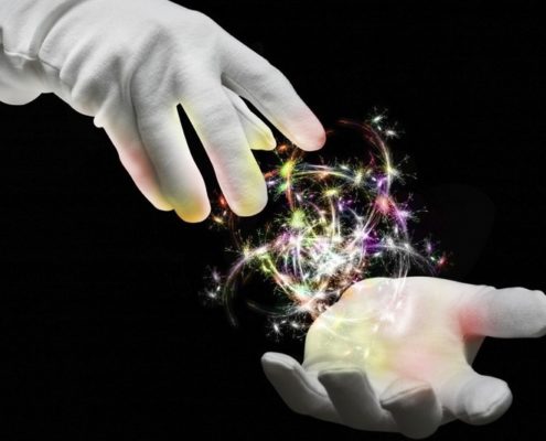 Two white gloved magician hands with a ball of multi colored sparks in between them against a dark black background
