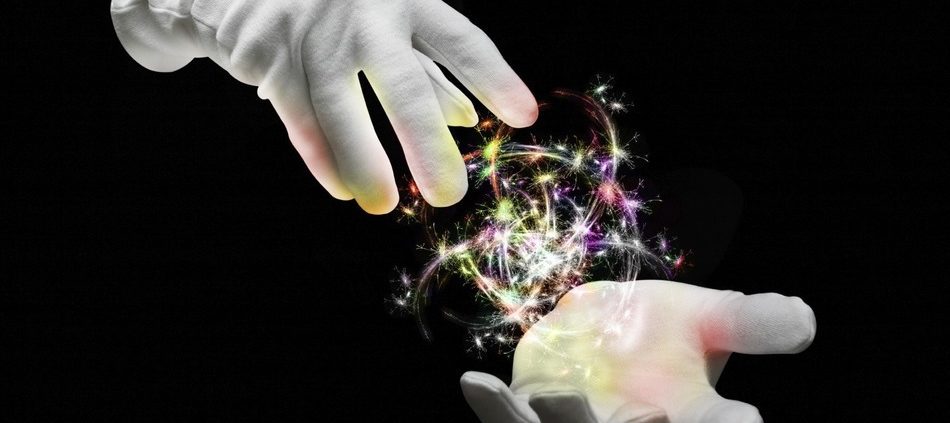Two white gloved magician hands with a ball of multi colored sparks in between them against a dark black background