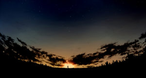 A fisheye style photo of the night sky with stars, clouds and the sun setting