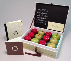 Custom presentation box for teacher appreciation with a chalkboard style writing on the inside of the lid and green and red apples in the box with a card and booklet next to it