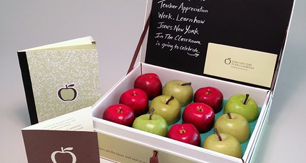 Custom presentation box for teacher appreciation with a chalkboard style writing on the inside of the lid and green and red apples in the box with a card and booklet next to it