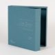 Dark teal colored turned edge binder box with black siding and white elegant style writing on the front