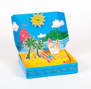 Beach themed pop up mailer opened with palm trees, surfboards, an island, a sailboat, and sun printed on the box and popout inserts