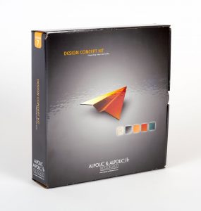 Dark grey product mailer box standing up with orange paper airplane on the front